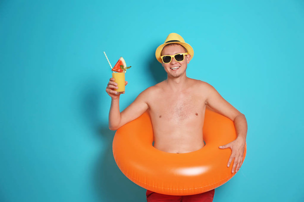 Shirtless man with inflatable ring and glass of cocktail on color background - Fotó, kép