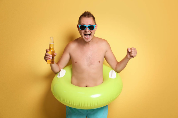 Shirtless man with inflatable ring and bottle of drink on color background - Foto, afbeelding