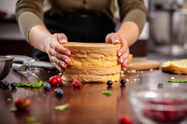 The pastry chef prepares a biscuit cake in the home kitchen or in a restaurant. The concept of the process of making cakes for restaurants, cafes and bars. on the photo the girl hands cuts a biscuit - Foto, Bild
