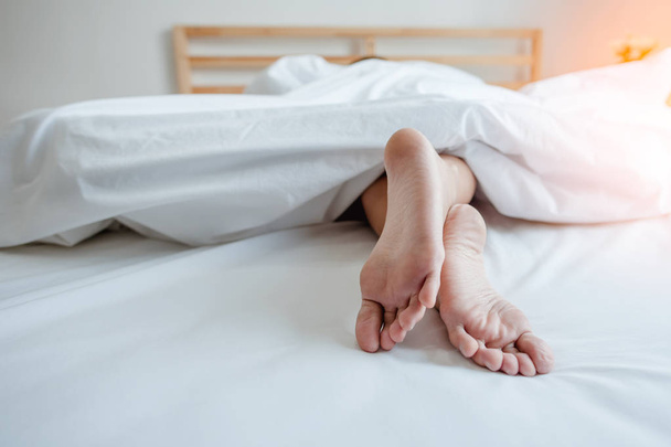 Young female sleeping in bed at home with focus on legs. Feet of woman lying on bed. - Foto, Imagem