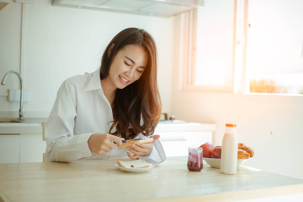 Asian woman slicing jam bread in the morning.feeling happy and fresh.Making breakfast meal in kitchen room. - 写真・画像
