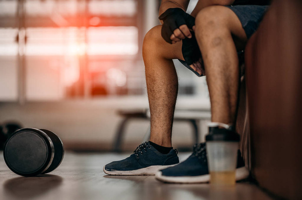 Muscular man at gym taking a break from workout sitting beside the bottle of mineral salt and dumbbells . - Fotografie, Obrázek