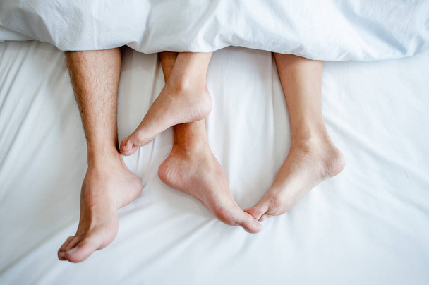 Love lying in bed in hotel,embracing on white sheets, close up legs. - Photo, Image
