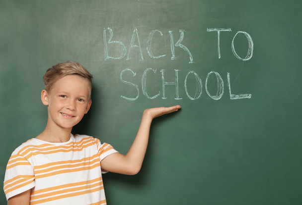 Little child near chalkboard with text BACK TO SCHOOL - 写真・画像