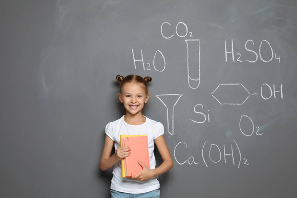 Little child with school supplies and chemical formulas on grey background - Photo, Image