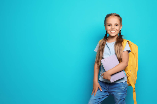 Little school child with backpack and copybook on color background - Fotoğraf, Görsel