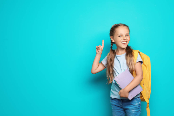 Little school child with backpack and copybook on color background - Foto, Imagen
