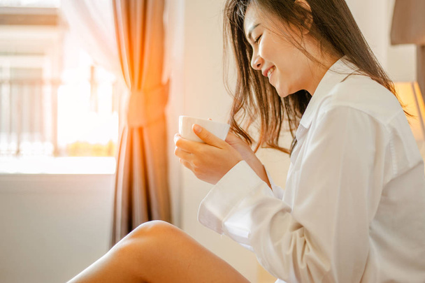 Woman holding a cup of coffee in her hands.Woman drinking coffee in bed at home with sunrise at window. - Foto, Bild