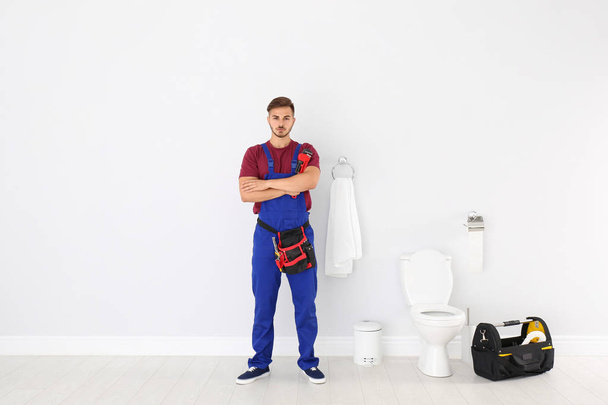 Young man with plumber wrench near toilet bowl in bathroom - Foto, afbeelding
