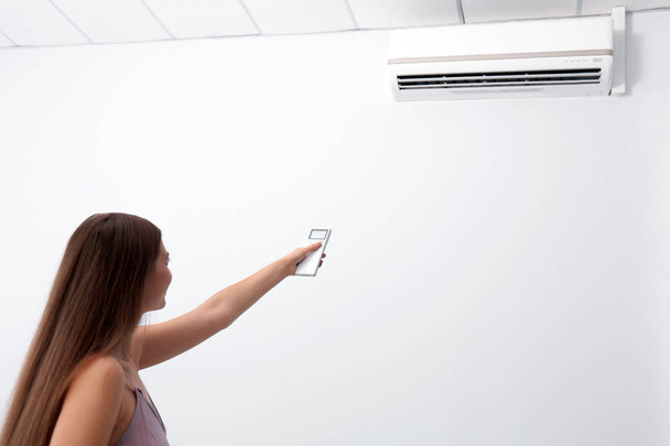 Woman operating air conditioner with remote control indoors - Foto, immagini