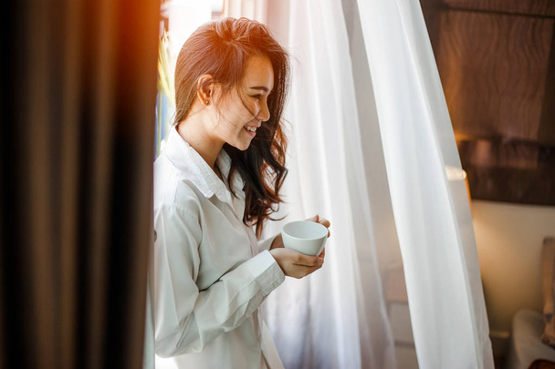 Woman holding a cup of coffee in her hands.Woman drinking coffee at home with sunrise at  window . - Foto, Bild