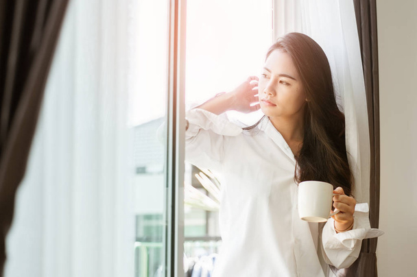 Frau mit einer Tasse Kaffee in der Hand. Frau trinkt Kaffee zu Hause mit Sonnenaufgang am Fenster . - Foto, Bild