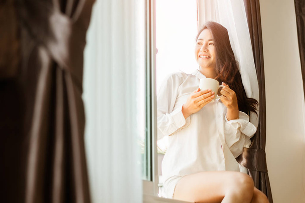 Nő kezében egy csésze kávé.Nő iszik kávét otthon napfelkeltével az ablakban . - Fotó, kép