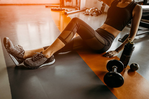 Relaxing after training.young woman sitting with dumbbell and protein shake bottle at gym.young female at gym taking a break from workout. - Foto, Imagen