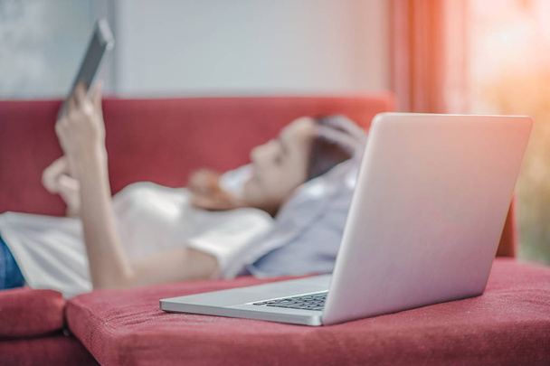 Happy young woman with tablet laying on sofa and  have a laptop. - Фото, зображення