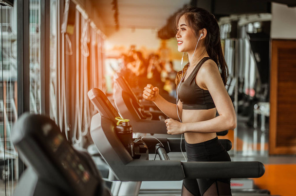 Portrait of Fitness woman running on treadmill in gym listening to music.exercising concept.fitness and healthy lifestyle. - Fotó, kép