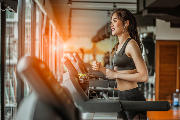 Portrait of Fitness woman running on treadmill in gym listening to music.exercising concept.fitness and healthy lifestyle. - Фото, изображение