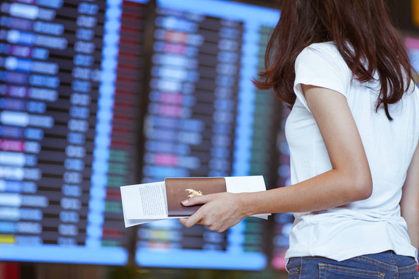  Meisje op internationale luchthaven met paspoort en instapkaart in de buurt van vlucht informatiebord - Foto, afbeelding