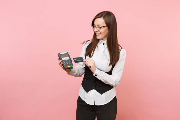 Молодая улыбающаяся деловая женщина с беспроводным современным банковским платежным терминалом для обработки и приобретения платежей по кредитным картам, черная карта изолирована на розовом фоне. Леди-босс. Достижение карьерного богатства
 - Фото, изображение