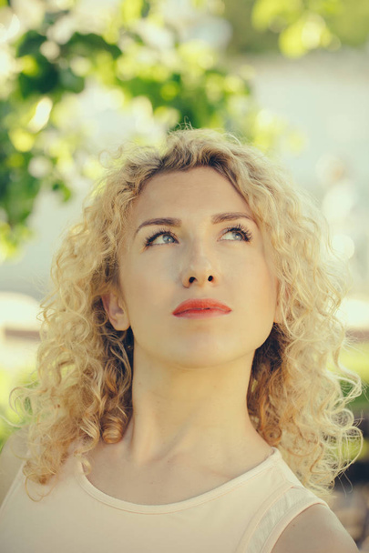 Girl with curly blond hair looking up on sunny r day - Fotó, kép