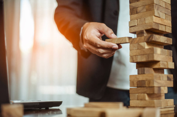 business man hand  pulling out or placing wood block on the tower in modern office. plan and strategy in business. blur for background. - Φωτογραφία, εικόνα