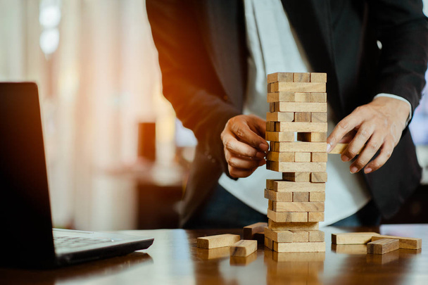 business man hand  pulling out or placing wood block on the tower in modern office. plan and strategy in business. blur for background. - Foto, Imagem