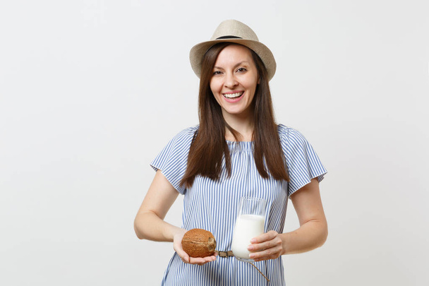 Giovane donna sorridente in tenuta vestito in mano latte di cocco in vetro, noce di cocco esotico isolato su sfondo bianco. Una corretta alimentazione, bevanda vegetariana vegana, stile di vita sano, concetto di dieta
. - Foto, immagini