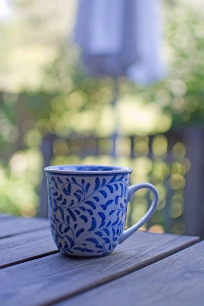 庭園の日陰で屋外の木製のテーブルにブルーの模様のマグカップ. - 写真・画像