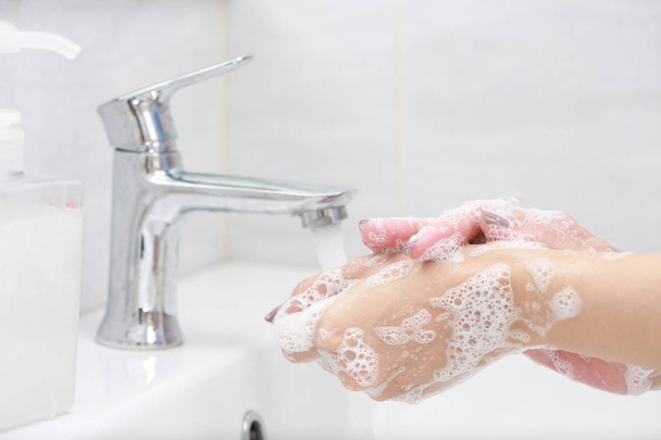 Πλένει τα χέρια με σαπούνι κάτω από τη βρύση με νερό. - Φωτογραφία, εικόνα