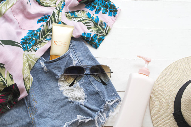 cosméticos naturais para pele rosto protetor solar spf50, óculos de sol, calças curtas jeans, loção corporal, chapéu e camisa da mulher relaxar verão no fundo branco de madeira
 - Foto, Imagem