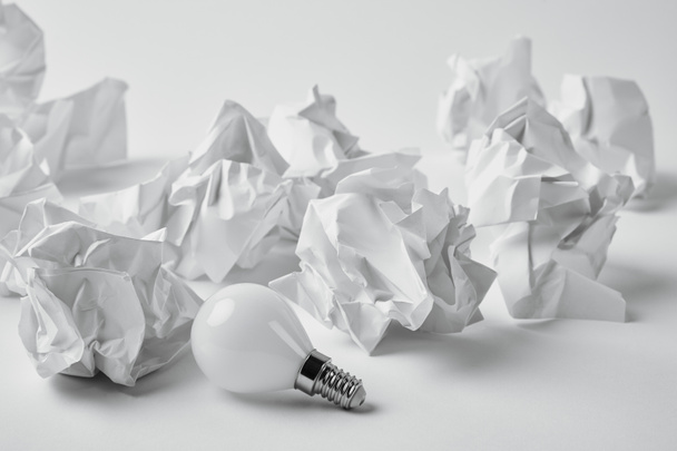 close-up shot of energy saving light bulb with crumpled papers on white - Photo, Image