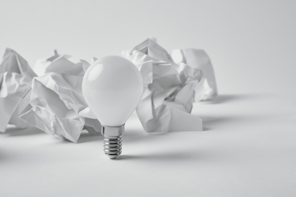 close-up shot of power saving light bulb with crumpled papers on white - Photo, Image