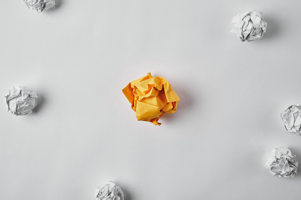 top view of crumpled yellow paper surrounded with white crumpled papers on white surface - Photo, image