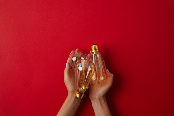 cropped shot of woman holding vintage incandescent lamps on red tabletop - 写真・画像