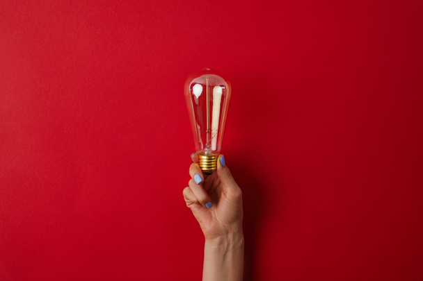 cropped shot of woman holding vintage incandescent lamp on red surface - Фото, изображение