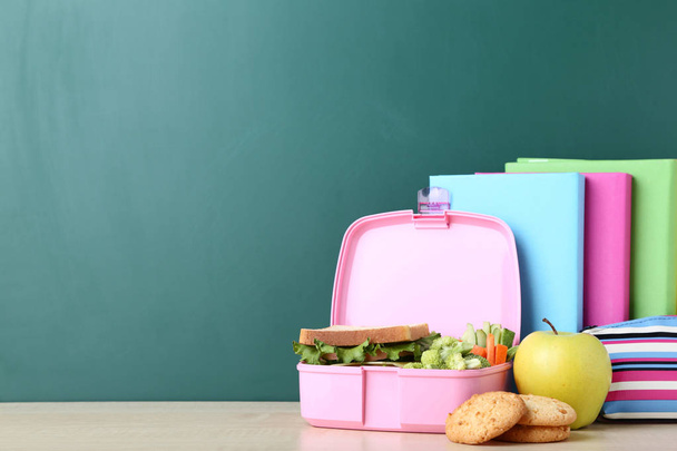 School lunch box with sandwich and colorful books on chalkboard background - Фото, изображение