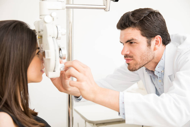 Привлекательный офтальмолог в лабораторном халате осматривает глаза молодой женщины на предмет очков в лаборатории.
 - Фото, изображение