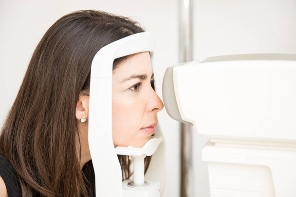 Retrato de una hermosa mujer mirando a la máquina hendidura lam apoyando la cabeza en el soporte durante las pruebas visuales en la oficina del optometrista
 - Foto, imagen