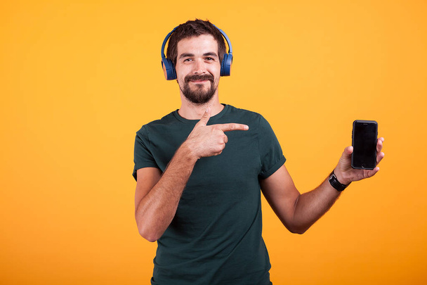 Happy joyful man wearing headphones and pointing at his smartphone - Photo, Image