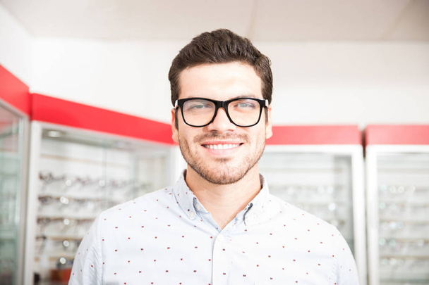Ritratto di un bell'uomo con gli occhiali che guarda la macchina fotografica mentre è in piedi nel negozio di ottica
 - Foto, immagini