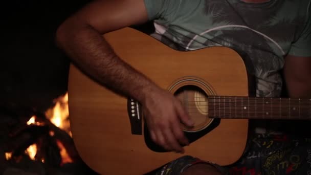 Een man is het spelen van gitaar op de achtergrond van een brand. - Video