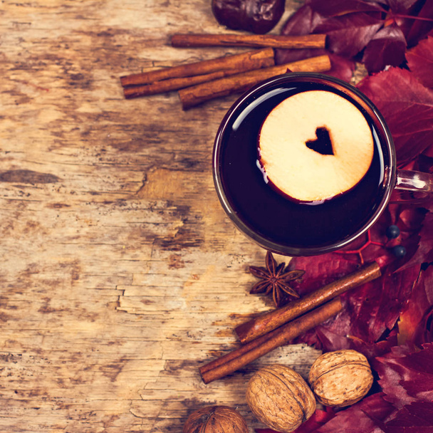 Hot Mulled wine with spices and fruits on an old wooden background. Autumn leaves, nuts, cinnamon. Autumn background. Text space. - Photo, Image