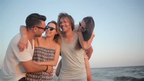Ενεργό τέσσερις ανθρώπους που περπατούν στην παραλία στις καλοκαιρινές διακοπές δαπάνες χρόνο μαζί κατά τη διάρκεια της φυσάει αέρας και απολαμβάνοντας το ηλιοβασίλεμα. - Πλάνα, βίντεο