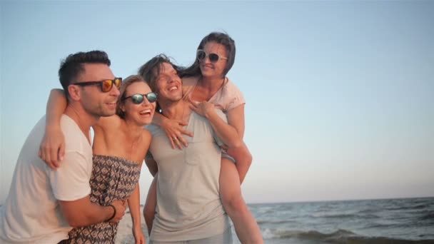 zwei Männer mit ihren erstaunlichen Freundinnen lächeln und lachen am Meer bei windigem Wetter am Abend, hd. - Filmmaterial, Video