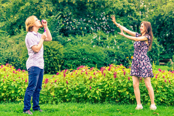 Happy funny hipster couple playing together blowing soap bubbles outdoor in spring park. - Foto, imagen