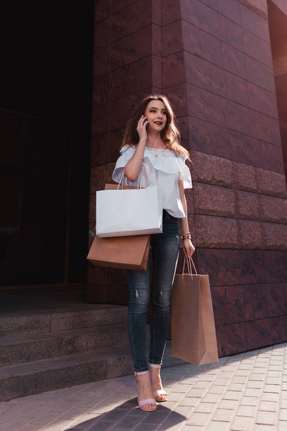 schöne, stylische junge Frau mit Einkaufstaschen, die aus dem Einkaufszentrum auf der Stadtstraße läuft und telefoniert. Schwarzer Freitag. Verkauf - Foto, Bild
