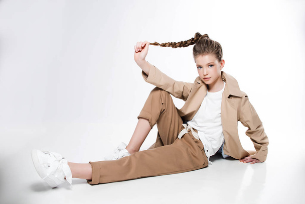 Young girl in beige trench sitting on white background - Foto, afbeelding