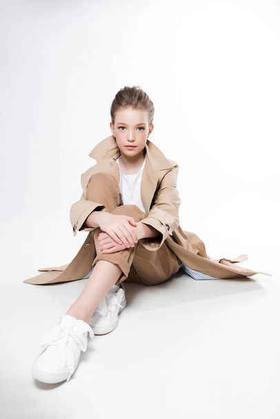 Young girl in beige trench sitting on white background - Фото, зображення