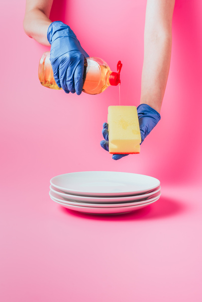 ピンクの背景の白いプレートのスタックは、スポンジを洗浄の食器洗い液体を注ぐゴム手袋での女性のイメージをトリミング、 - 写真・画像