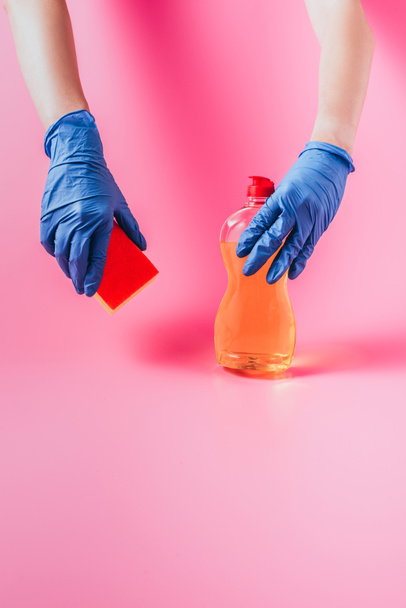 image recadrée de la femme en gant de caoutchouc tenant éponge de lavage et liquide vaisselle, fond rose
  - Photo, image